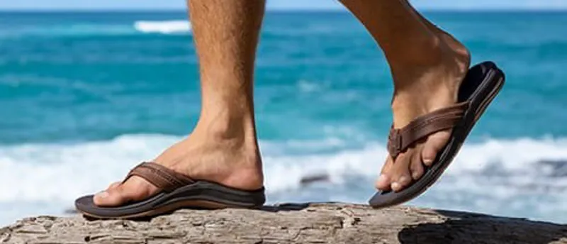 Brown Reef flip flops worn by a man walking on wood